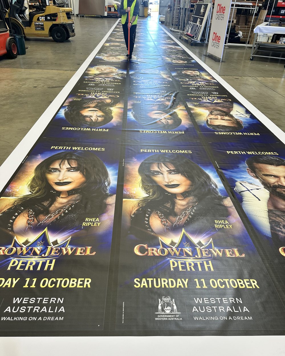 A long run of printed event banners laid out on the production floor at the Maddington workshop